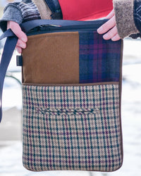 A person holding a patchwork shoulder bag outdoors. The bag features a brown suede-like panel, a blue and purple plaid section, and a beige plaid lower section with a front pocket.