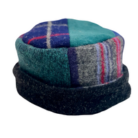A patchwork wool cap featuring a teal and blue plaid pattern on top, a teal and gray striped section on the front, and a dark navy ribbed brim, shown against a plain white background.