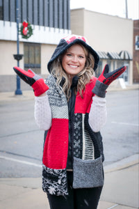 A woman smiling outdoors in a winter outfit featuring a red, black, and white hoodie scarf, coordinating knit mittens from baabaazuzu standing on a city street.