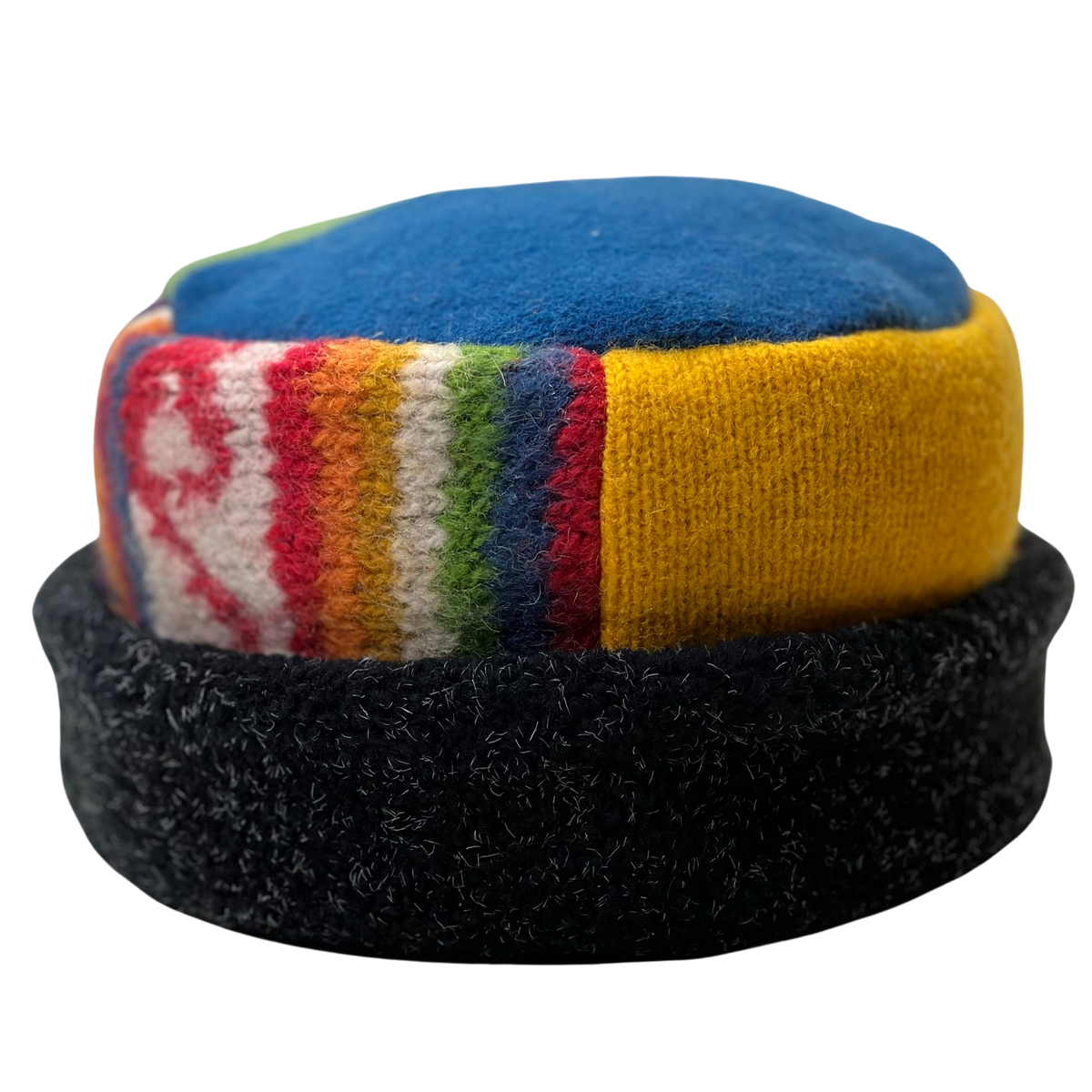 A handmade wool cap featuring a blue top panel, a yellow knit section, a multicolor striped patterned band, and a black fuzzy brim, shown against a plain white background.